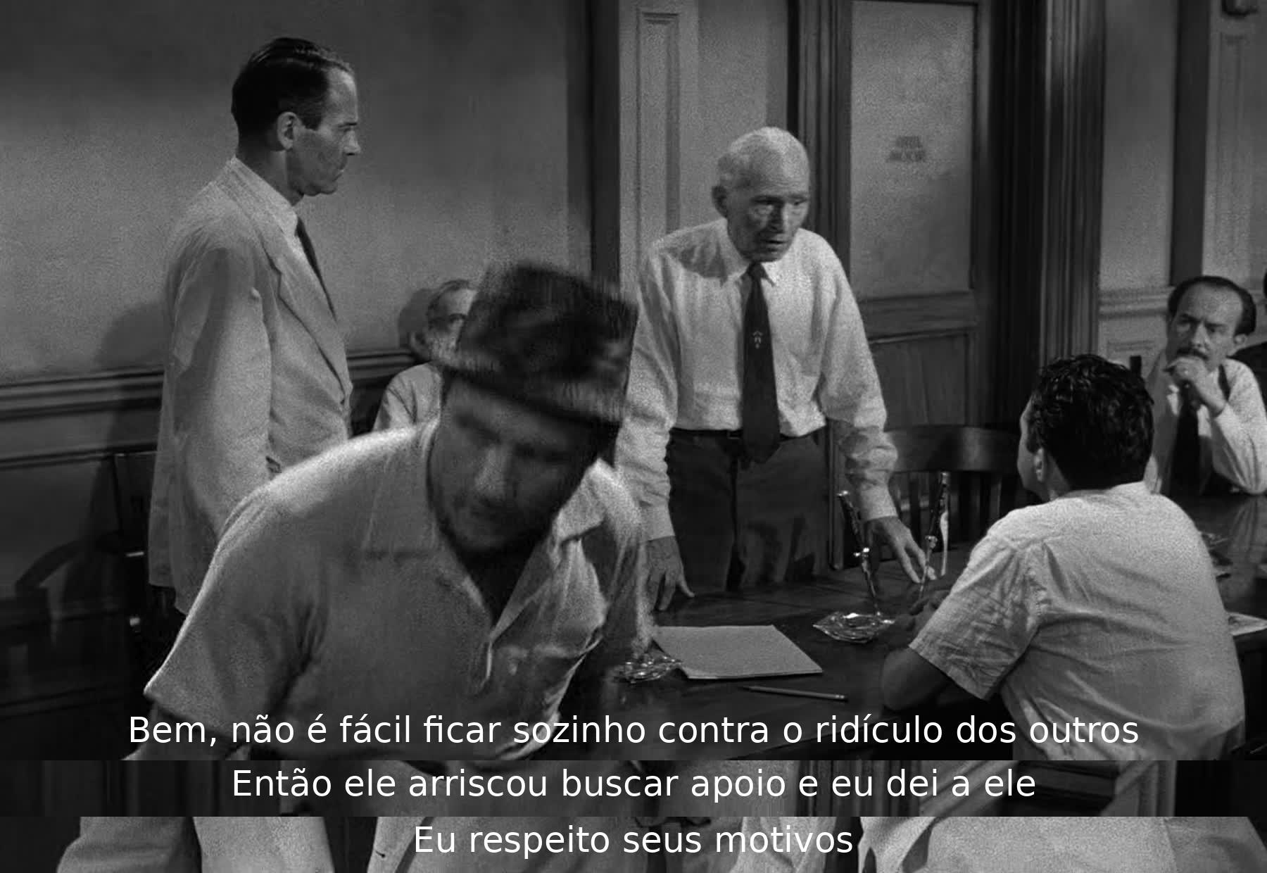 Um homem apoia outro que enfrenta o ridículo dos demais, oferecendo suporte e respeito aos motivos do colega.